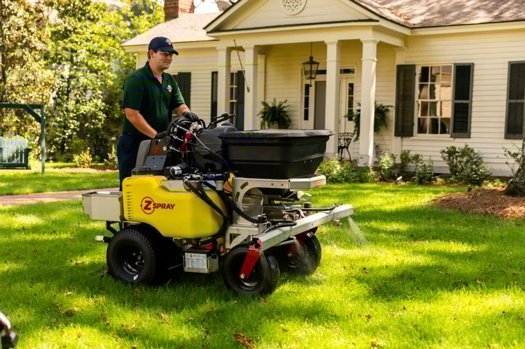lawn care technician on liquid sprayer machine applying treatment to lawn