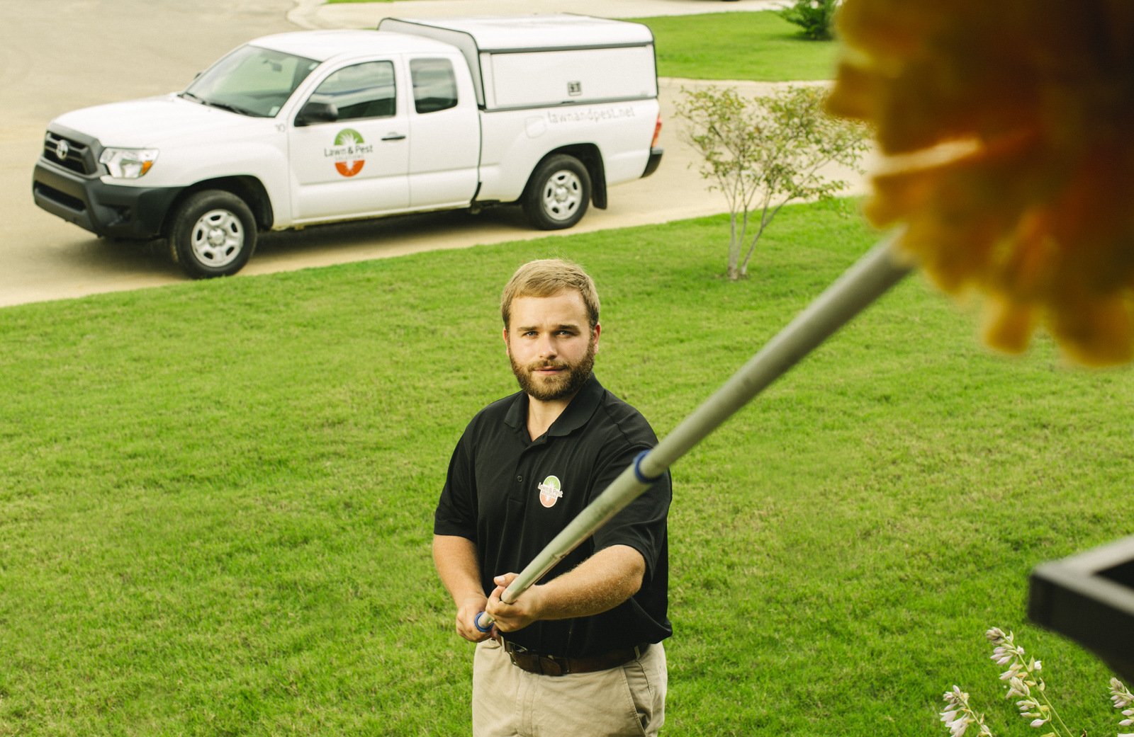 pest control technician sweeping house for spiders with truck in background