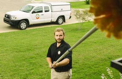 pest control technician sweeping house for spiders with truck in background